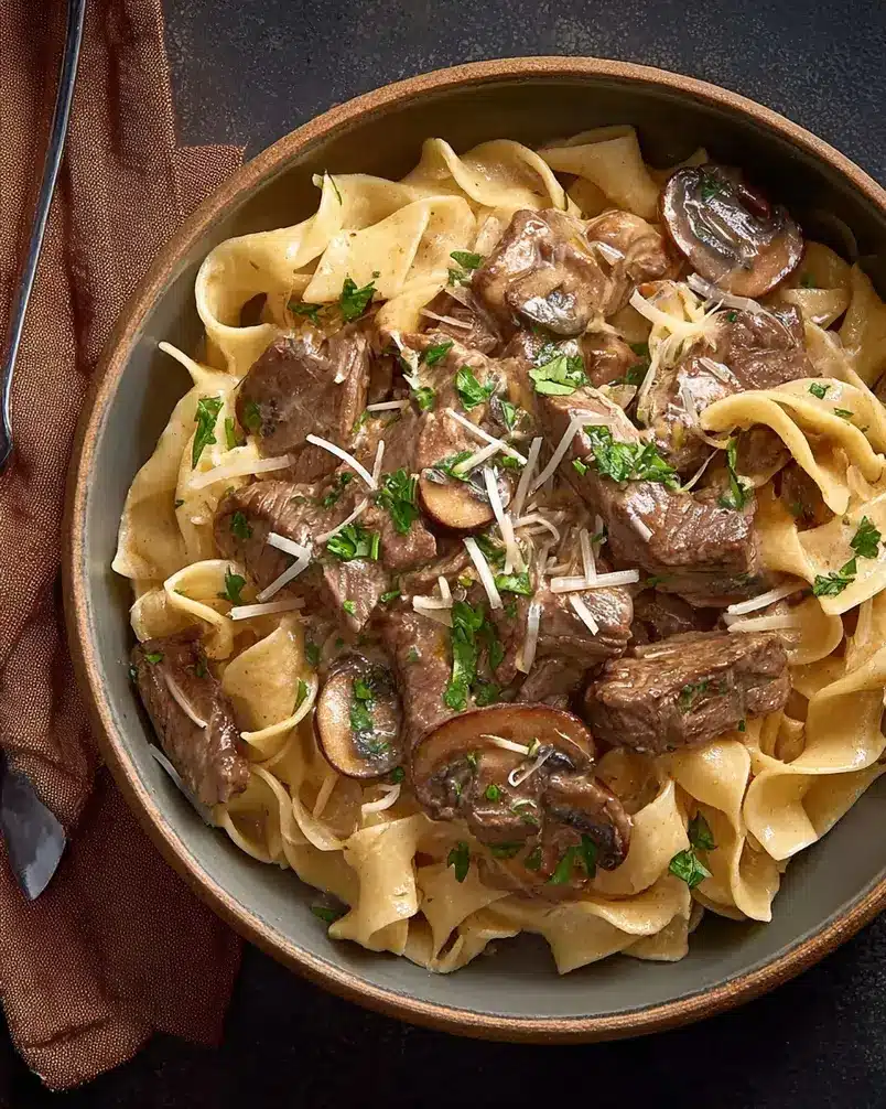 Beef Stroganoff 2 Recipe preparation image, showing ingredients like beef, onions, mushrooms, and sour cream laid out on a wooden surface.